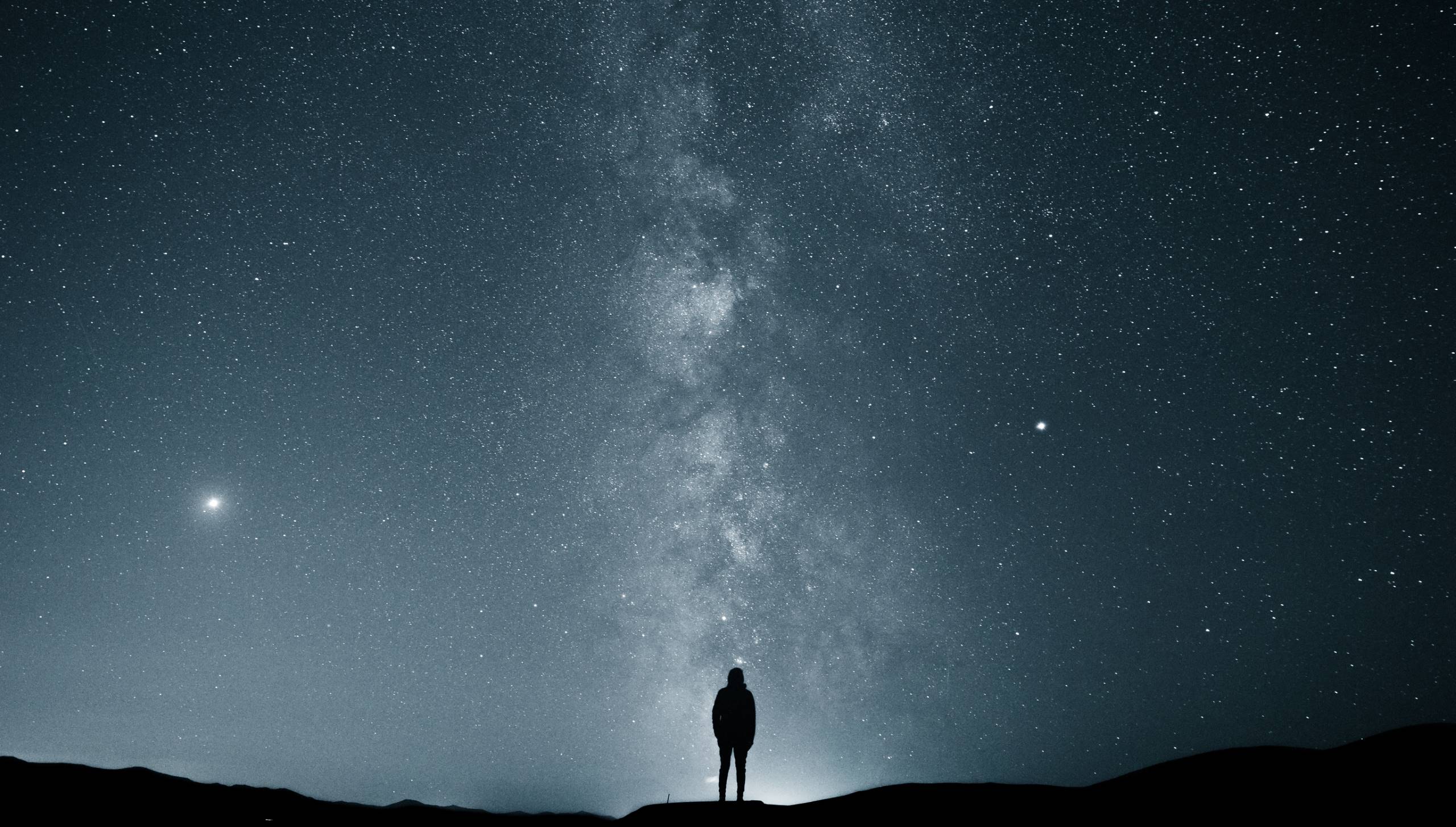 Silhouette einer Person unter einem klaren Sternenhimmel mit sichtbarer Milchstraße.